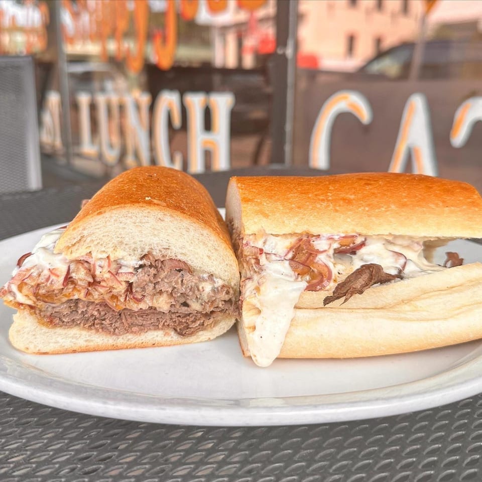 Two halves of a Mr. J's Deli cheesesteak sandwich with melted cheese and onions on a white plate.