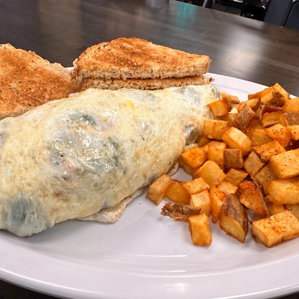 A Mr. J's Deli breakfast plate with a large omelet, crispy home fries, and two slices of toast.