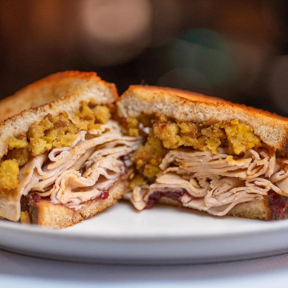 A Mr. J's Deli sandwich, cut in half, revealing layers of turkey and stuffing on toasted bread.