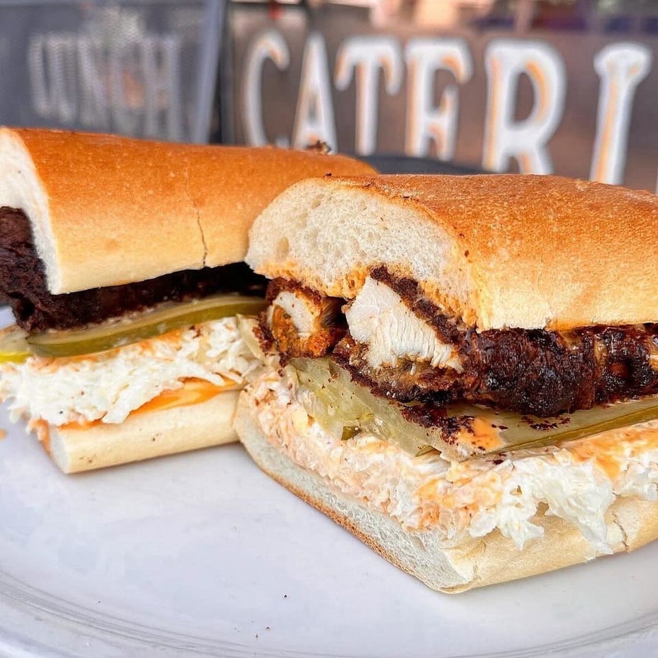 Two Mr. J's Deli sandwiches with fried chicken, coleslaw, and pickles on a white plate.