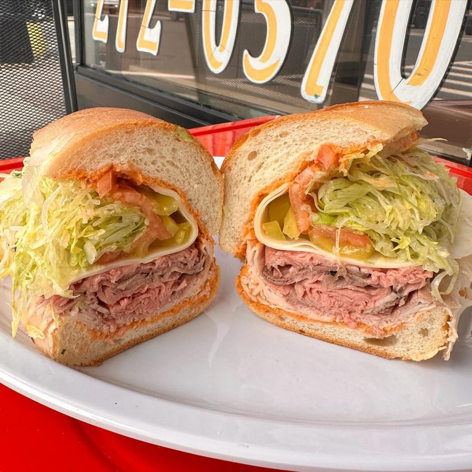 A large deli sandwich, cut in half, filled with meat, cheese, lettuce, and pickles.