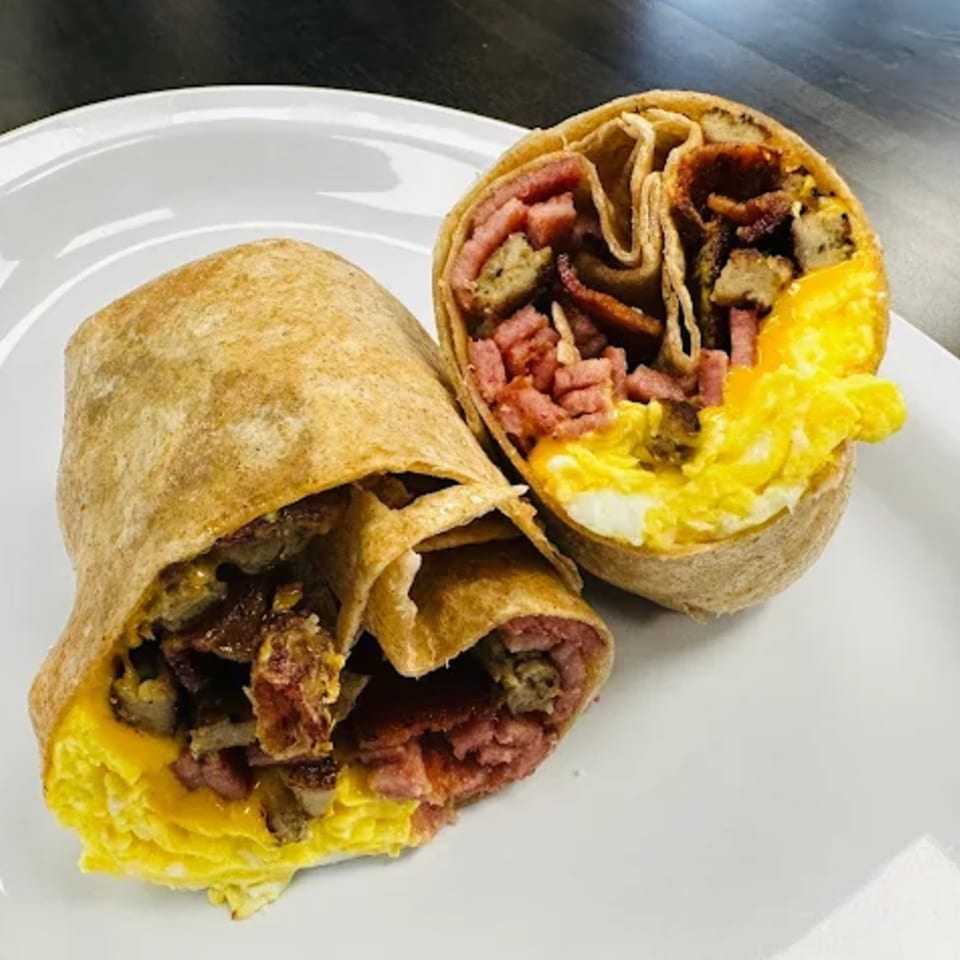 Two halves of a breakfast burrito filled with scrambled eggs, bacon, and sausage on a white plate.