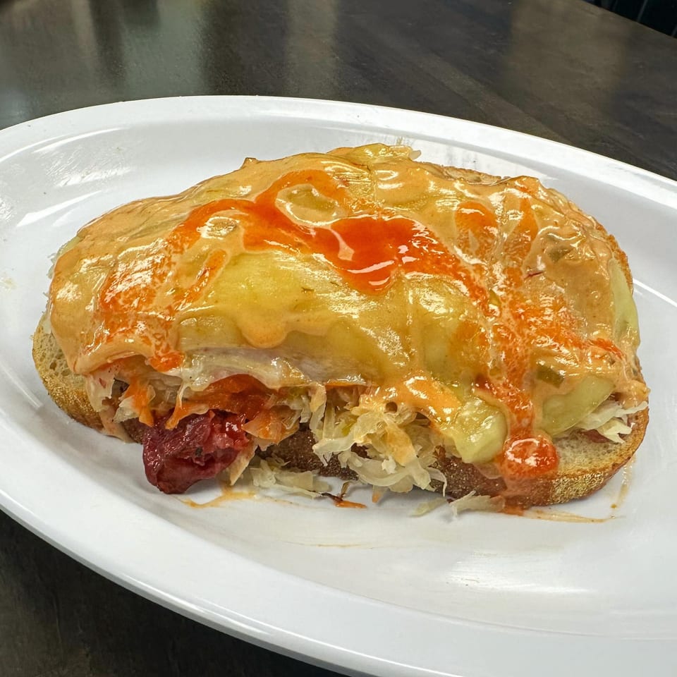 A Mr. J's Deli open-faced sandwich with melted cheese, sauerkraut, and sauce on a white plate.