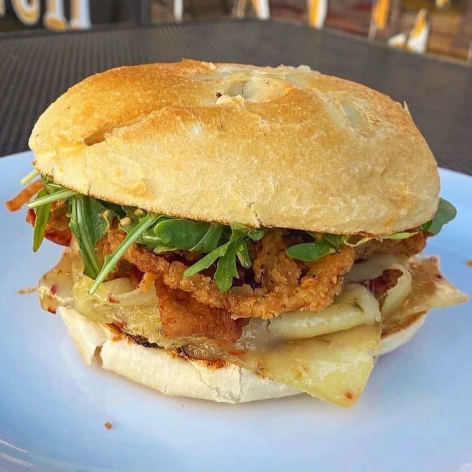 A Mr. J's Deli sandwich with crispy fried onions, melted cheese, and arugula on a bun.
